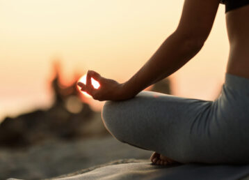 Close-up of woman meditating in lotus position at sunset.